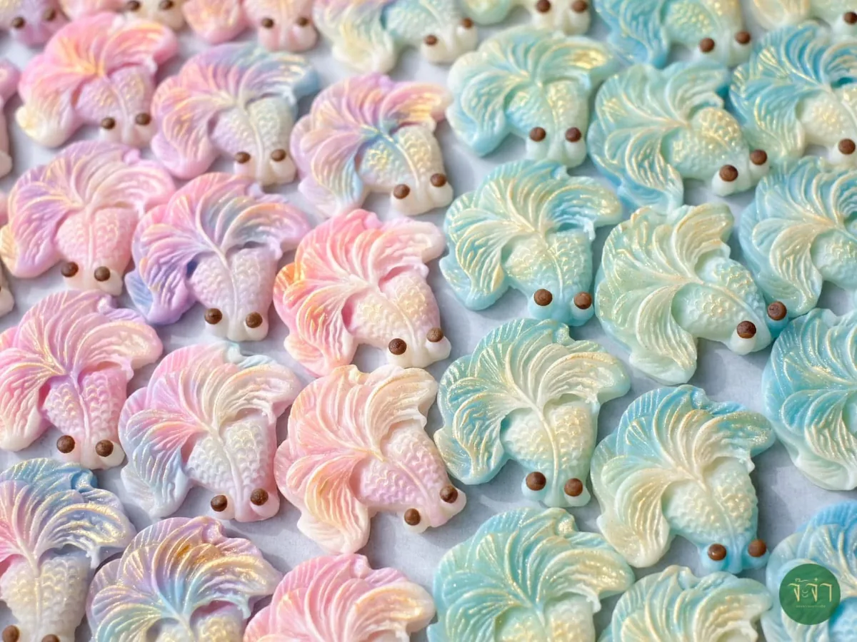 ขนมรูปปลากัดสีพาสเทลวางเรียงเต็มถาด ครึ่งหนึ่งไล่สีชมพูม่วง อีกครึ่งไล่สีฟ้าเขียว แต่ละตัวปั้นครีบและเกล็ดละเอียด มีจุดสีน้ำตาลเป็นตา