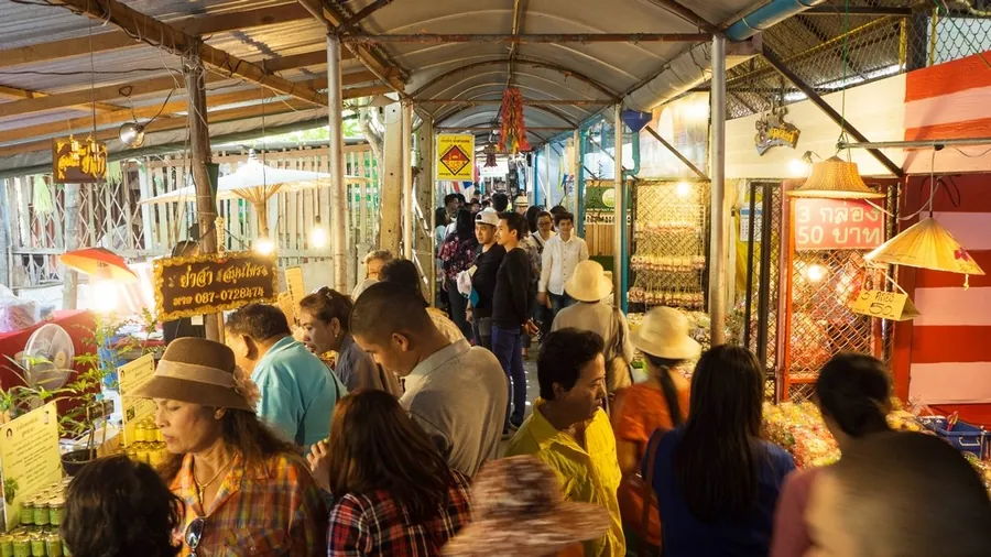 ทางเดินในตลาดที่มีหลังคาคลุม สองข้างเป็นแผงร้านค้า มีคนเดินเลือกซื้อของกันแน่นทาง