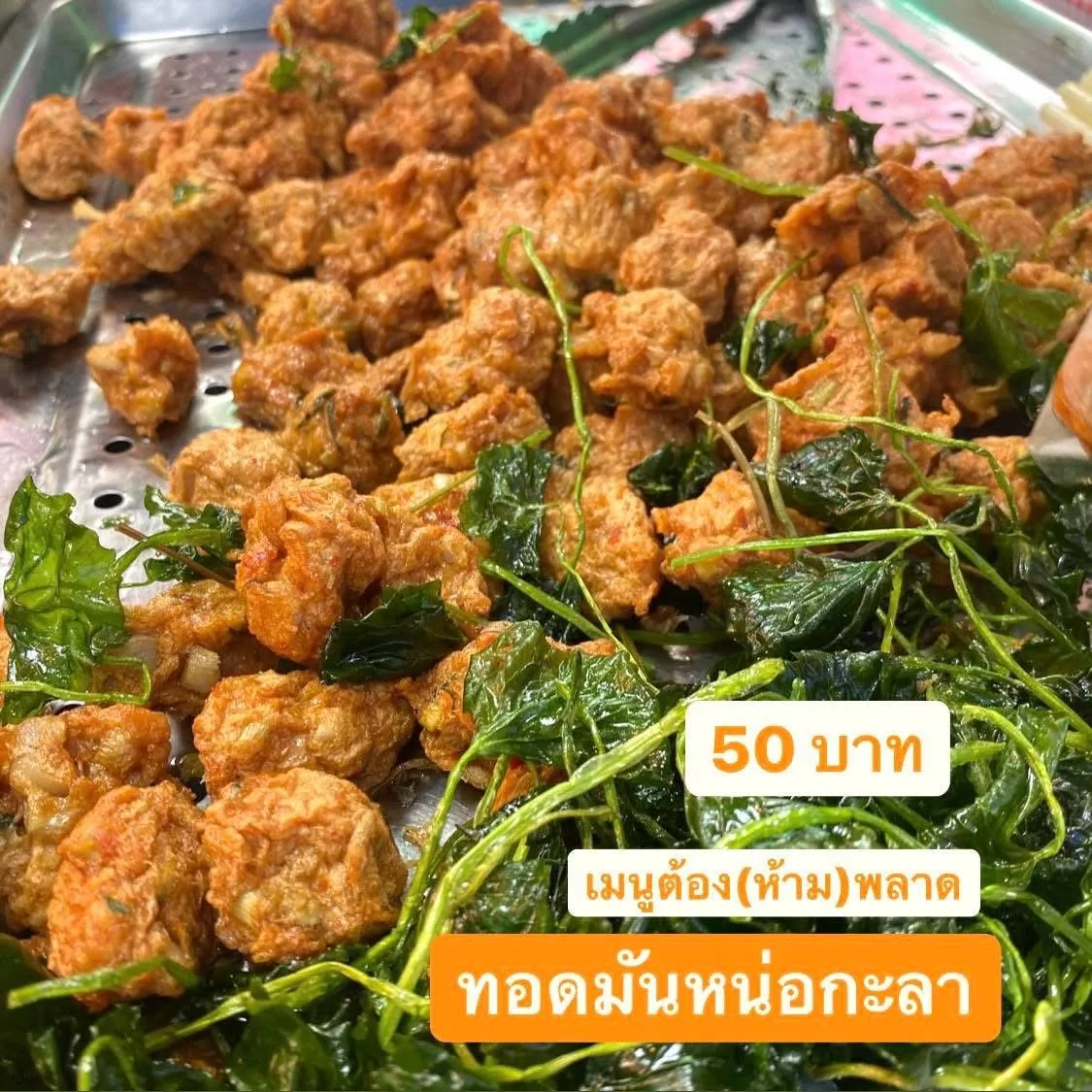 ทอดมันหน่อกะลาทอดสุกวางบนถาดสเตนเลสเจาะรู แทรกด้วยใบไม้เขียวทอดกรอบ มีข้อความบนภาพระบุราคา 50 บาท และคำว่าทอดมันหน่อกะลา