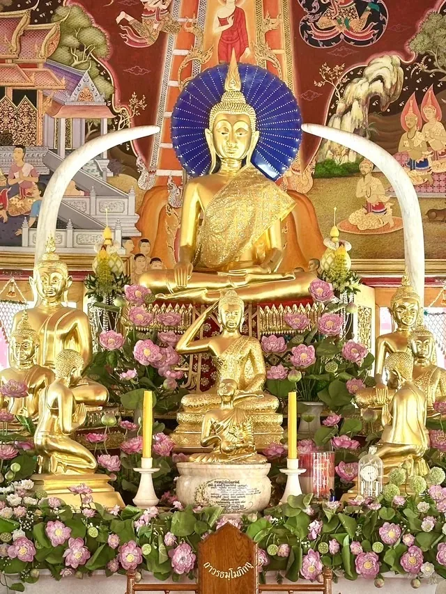 พระประธานสีทองในพระอุโบสถ มีงาช้างสีขาวโค้งขนาบสองข้าง ด้านหน้าเป็นแท่นบูชาที่ประดับดอกบัวสีชมพูและเทียนสองเล่ม